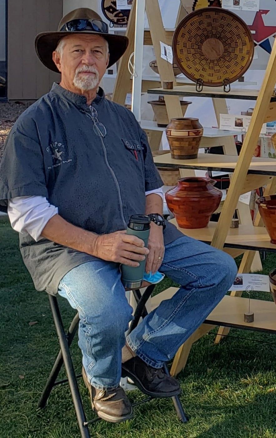 David Kohler seated beside a display of his turned wooden bowls and vessels at an outdoor art festival
