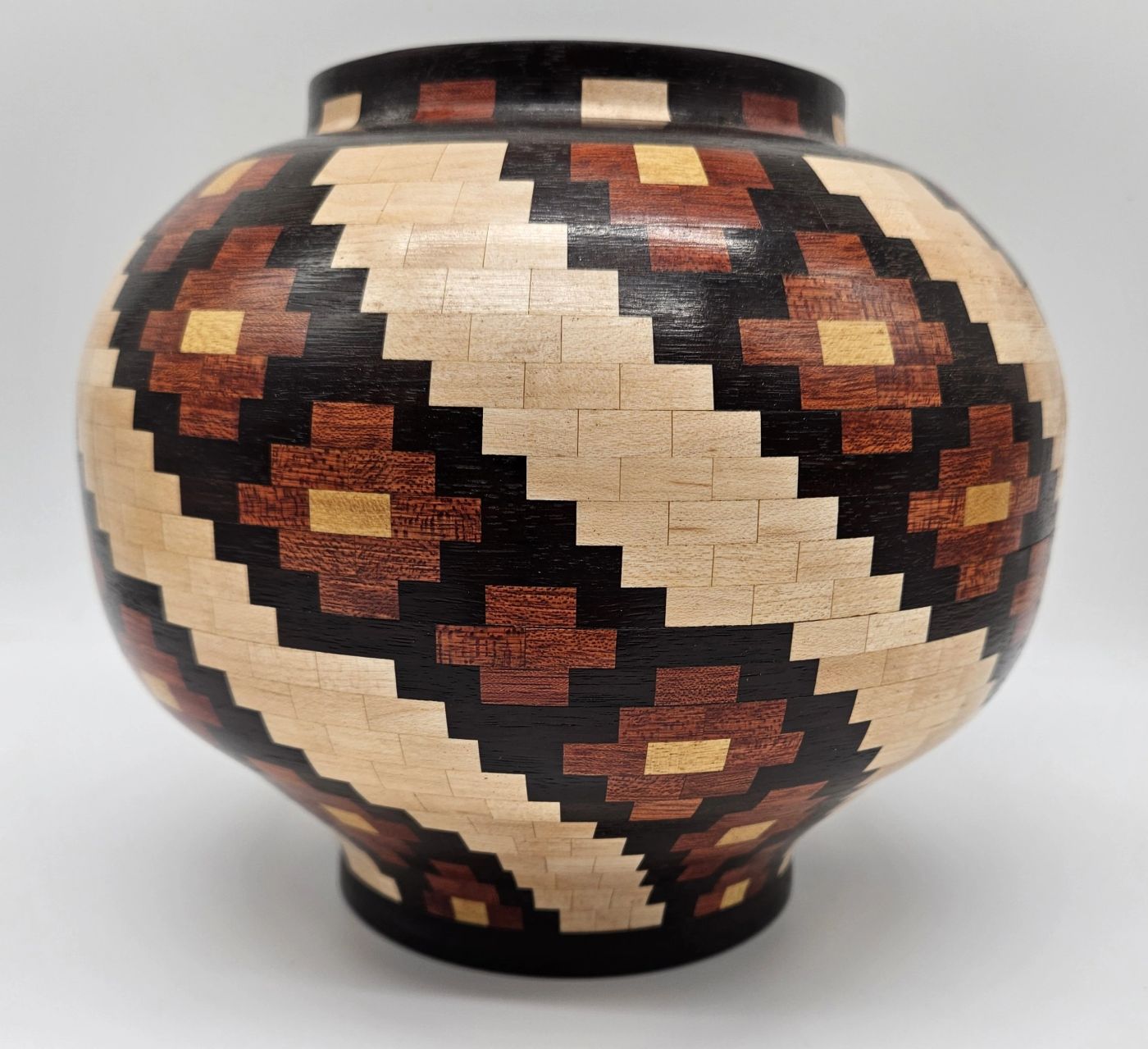 Rounded segmented wooden jar covered in a diagonal stepped diamond pattern of pale maple, red-brown and dark hardwood with small gold squares