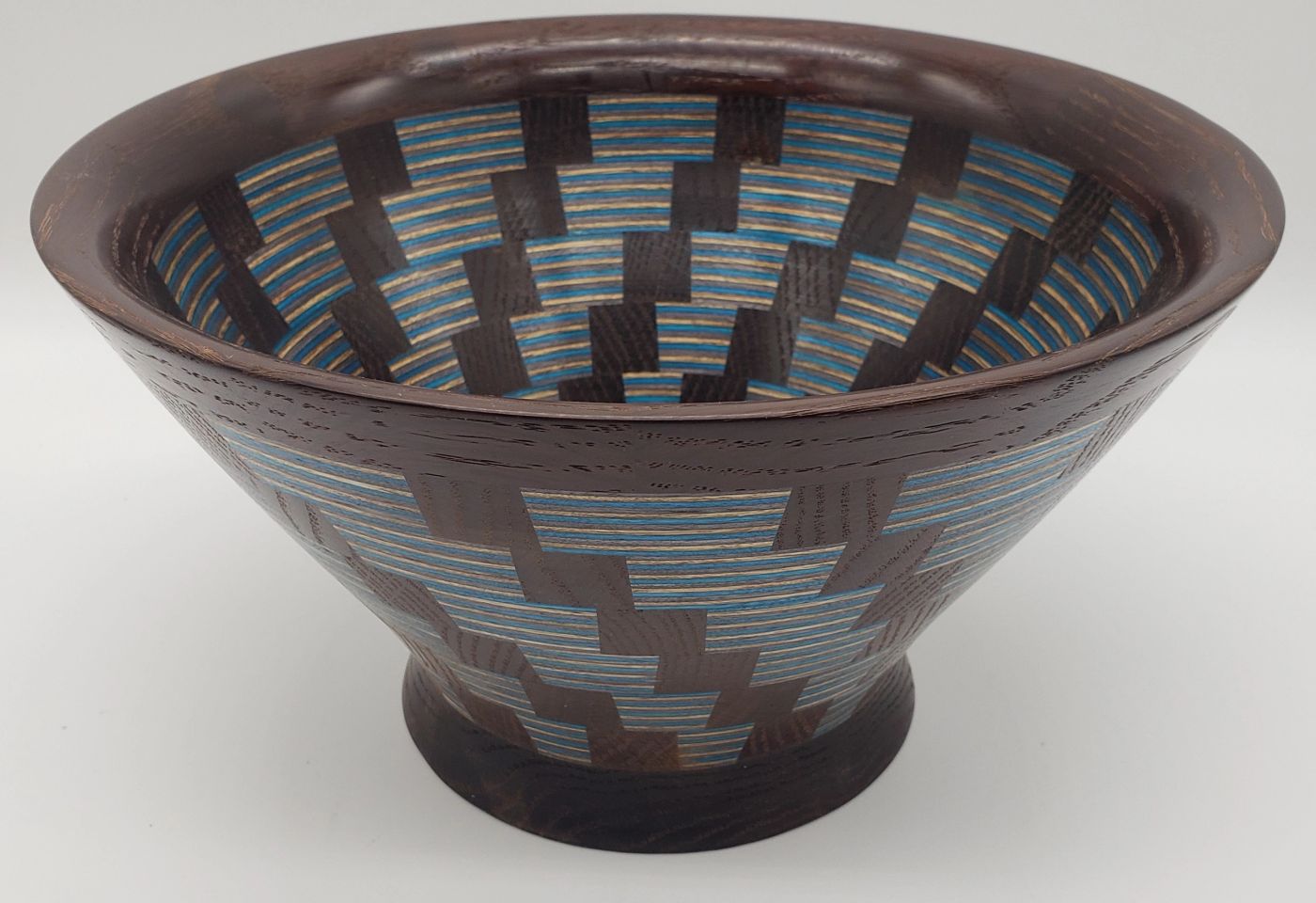 Flared segmented wooden bowl in dark hardwood with a stepped pattern in fine blue and cream dyed veneer lines