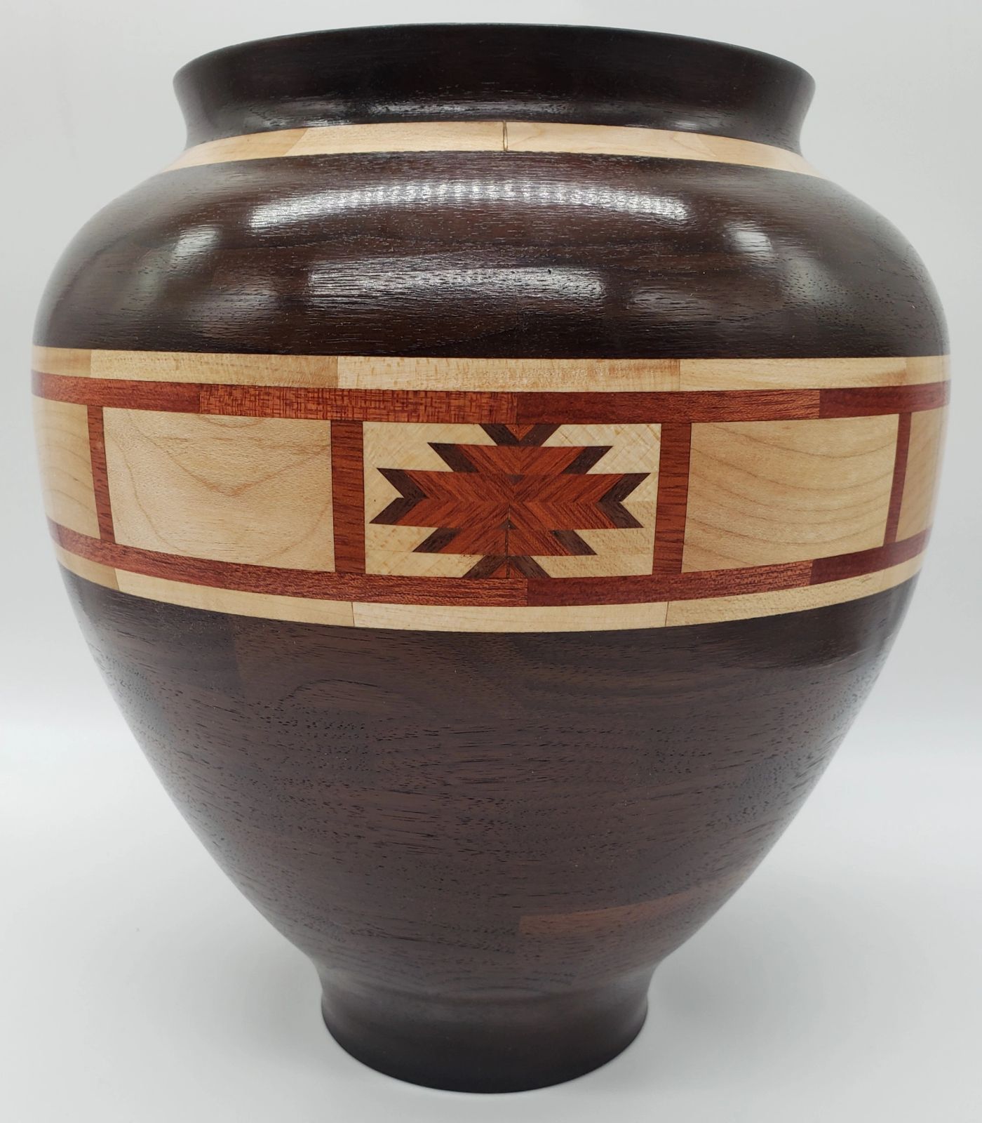 Dark segmented wooden jar with a wide pale maple band framing a red-brown stepped star motif