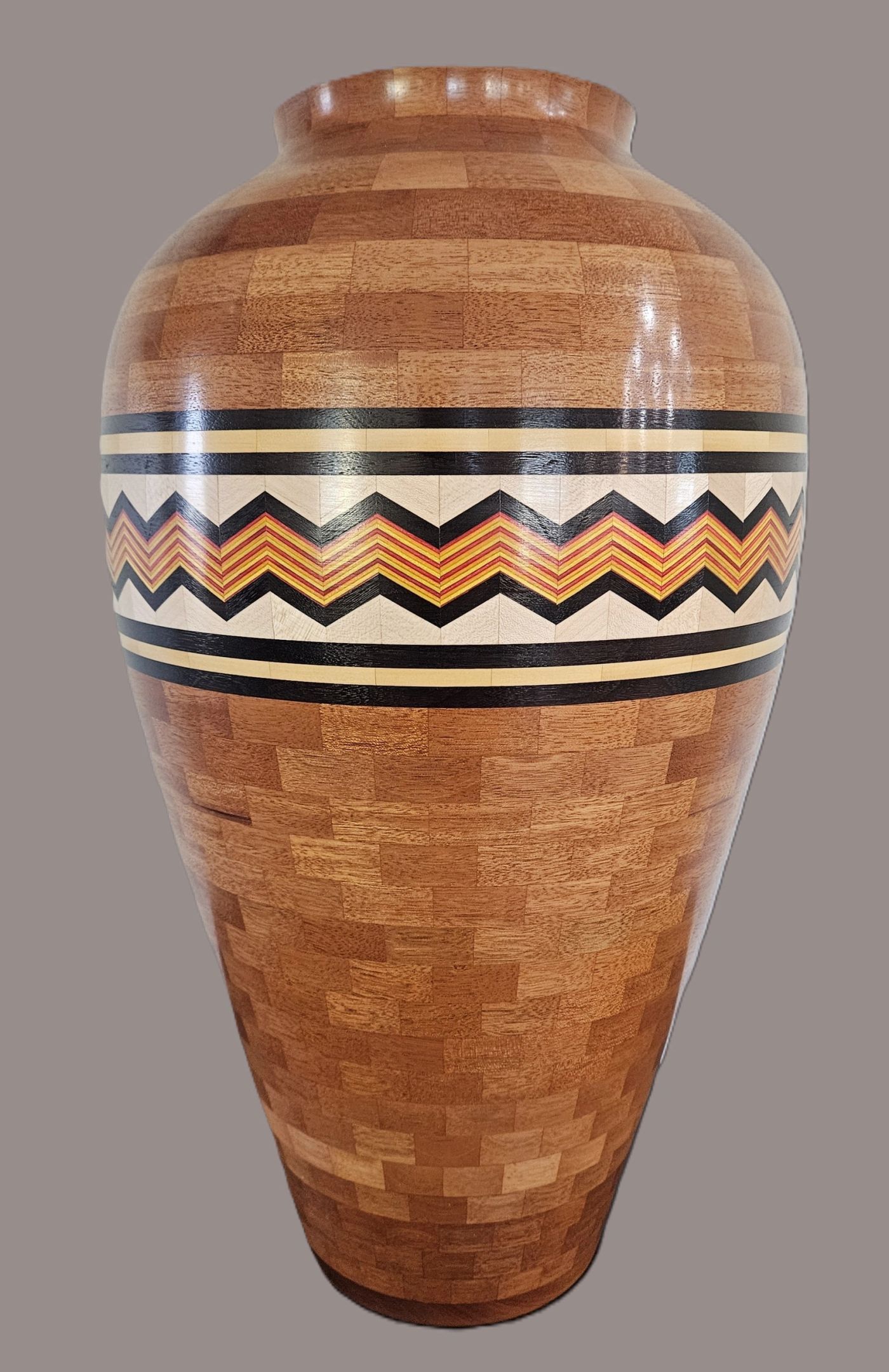 Tall segmented wooden vase in warm mahogany tones with a zigzag band of black, cream, red and yellow across the shoulder