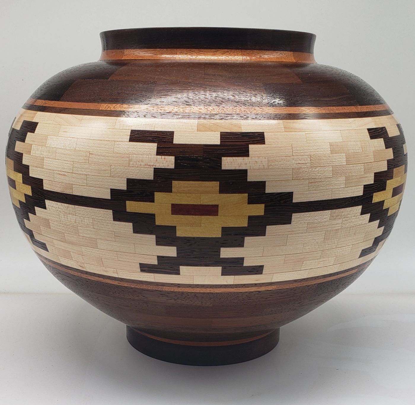 Wide segmented wooden vessel with dark rim and foot and a pale maple band holding a stepped geometric motif in dark brown, gold and red